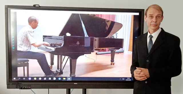 Сергей Исаков в классе школы и за роялем (на экране) в концертом зале Новгородского центра «Диалог».