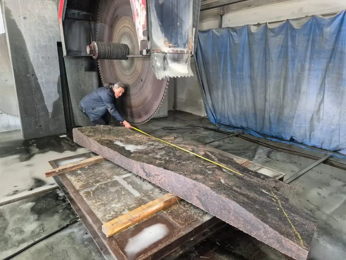 Скульптор размечает контуры стелы-крыла перед распилом камня.