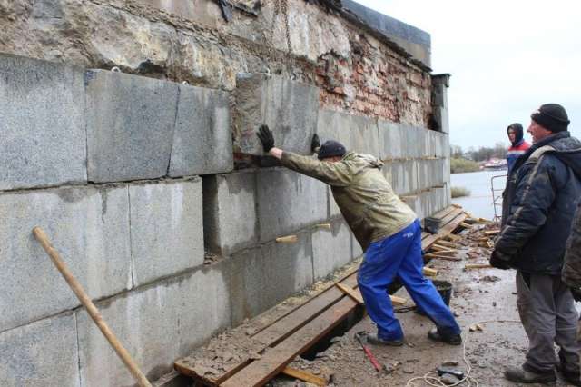 Рабочие восстанавливают облицовку из гранитных блоков.